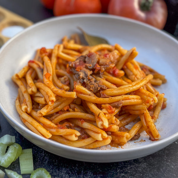 casarecce pasta dish with tomato sauce in a white bowl on a dark surface