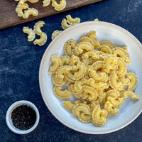 White plate with creste di gallo  pasta on a blue surface, small bowl of black pepper nearby.