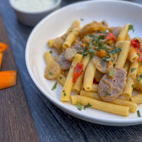 Sedani Pasta dish with sausage and vegetables on a white plate